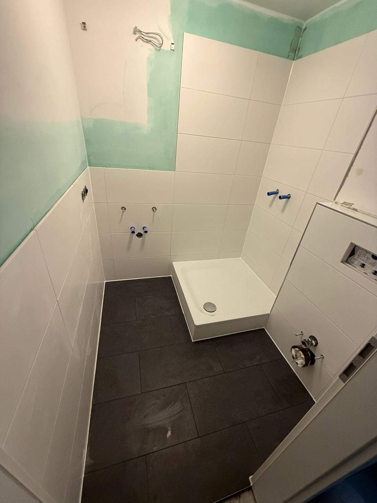 Badezimmer mit verlegten Wand- und Bodenfliesen sowie eingesetzter Duschwanne